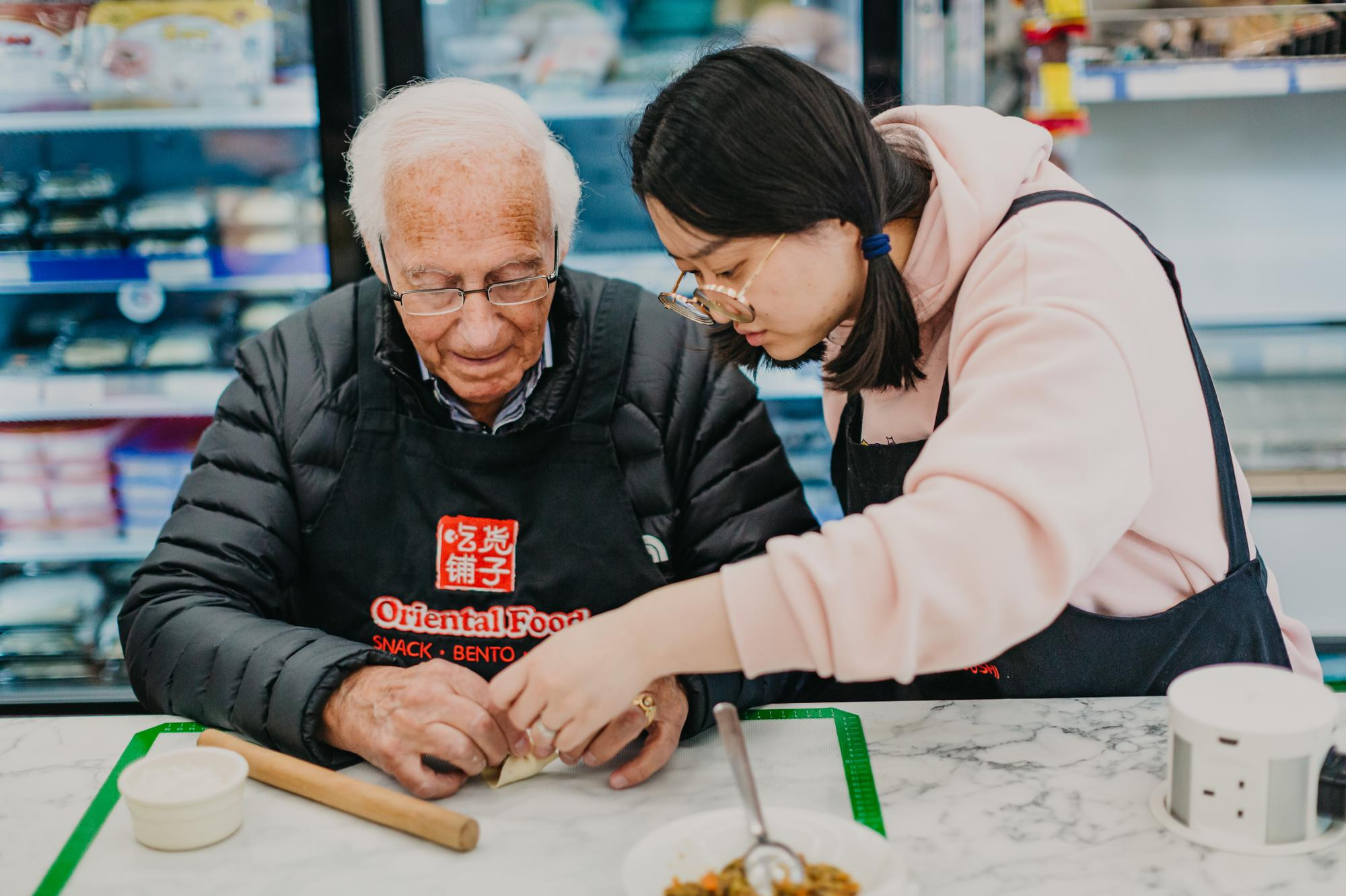 A woman helps an older man to assemble Chinese dumplings